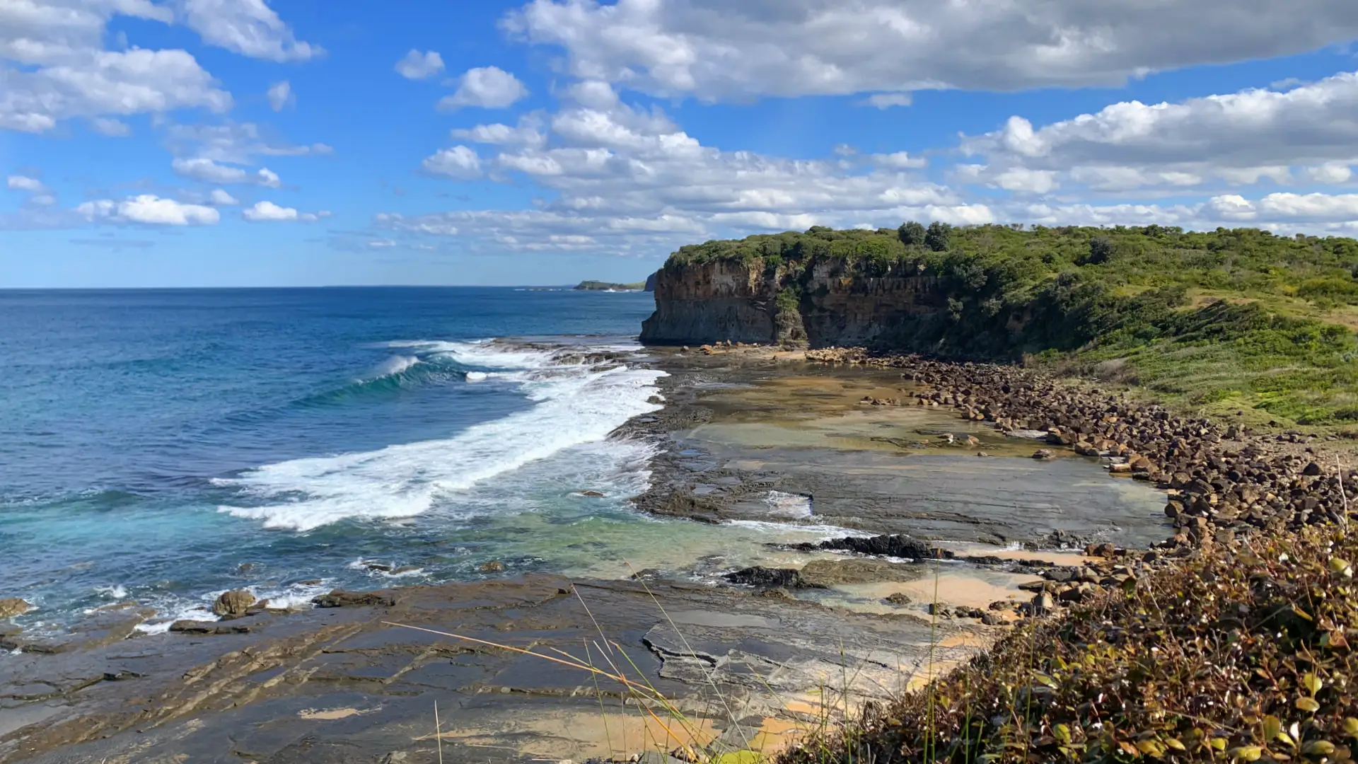 Waves coming into a bay with sea cliffs in the background along the Loves Bay to Werri Lagoon walk in Kiama.