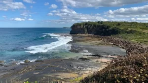 Waves coming into a bay with sea cliffs in the background along the Loves Bay to Werri Lagoon walk in Kiama.